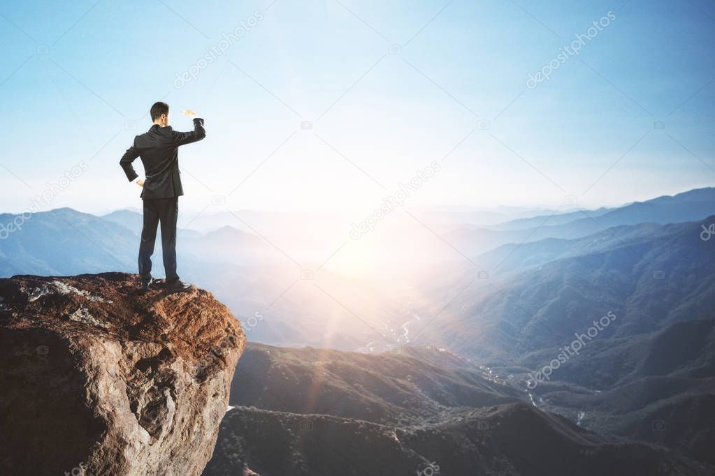 businessman staring into the distance from mountain cliff looking for solution