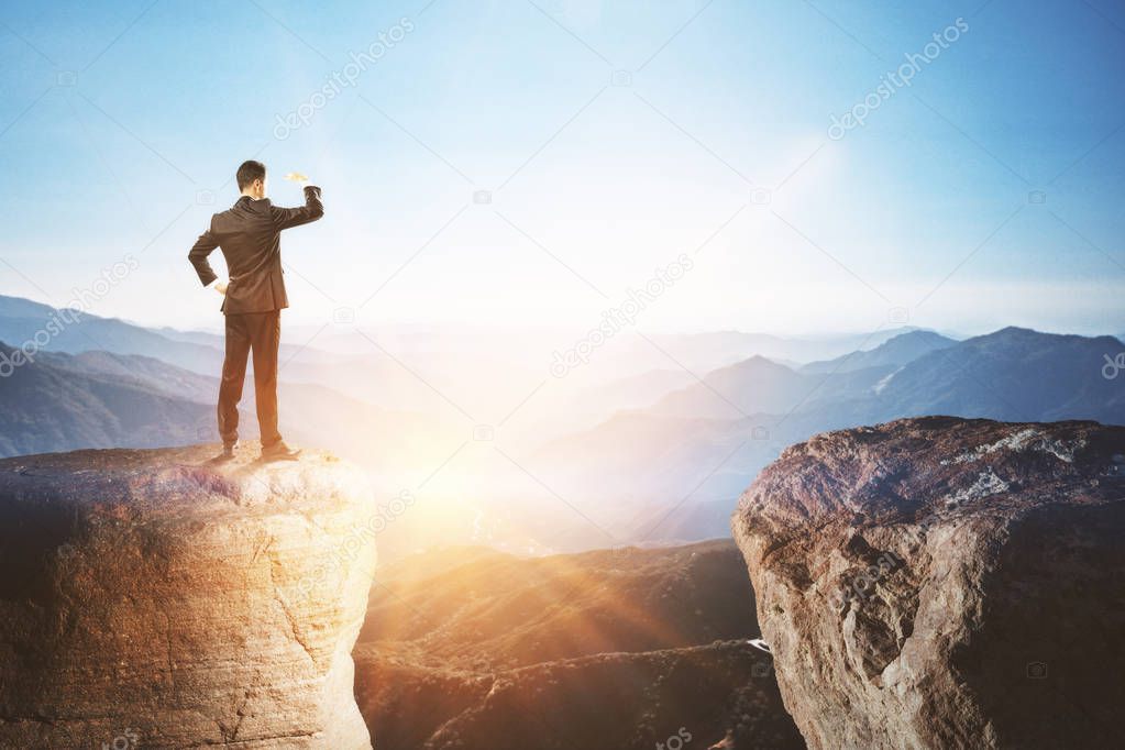 businessman staring into the distance from mountain cliff at dawn background