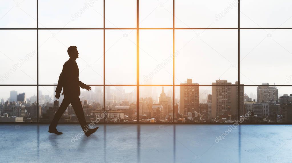 businessman walking in empty hall with megapolis city behind the window