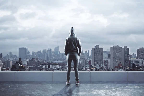 Female hacker with hood standing on rooftop with city view. Hacking and online concept
