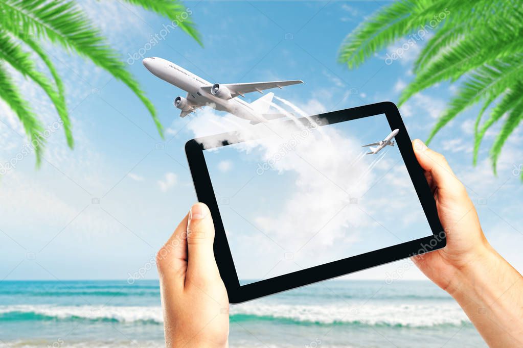 Hands holding tablet with abstract airplane on beautiful island beach background. Online booking and trip concept 