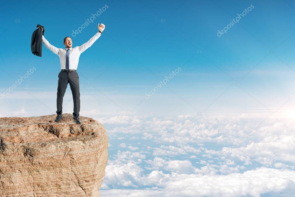 Businessman celebrating success on cliff edge. Sky background. Leadership and winner concept 
