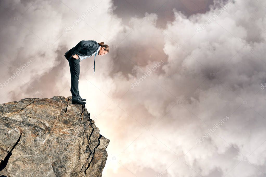 Businessman looking down from mountain top on sky background. Success and risk concept 