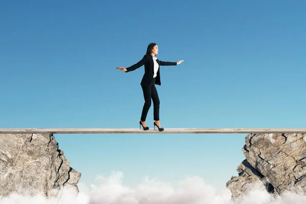 Young businesswoman balancing between two cliffs on blue sky background. Equilibrium concept