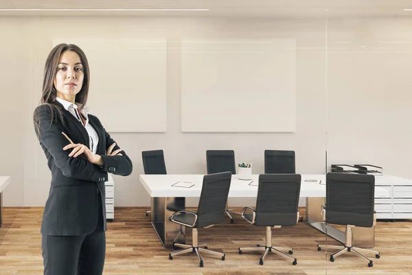Attractive businesswoman with folded arms standing in modern meetinr room interior.