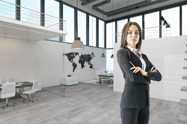 Confident businesswoman with folded arms standing in modern office interior.