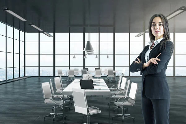Caucasian businesswoman with folded arms standing in modern office interior.