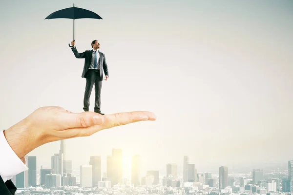 Große Hand Hält Jungen Geschäftsmann Mit Regenschirm Auf Hellem Stadthintergrund — Stockfoto