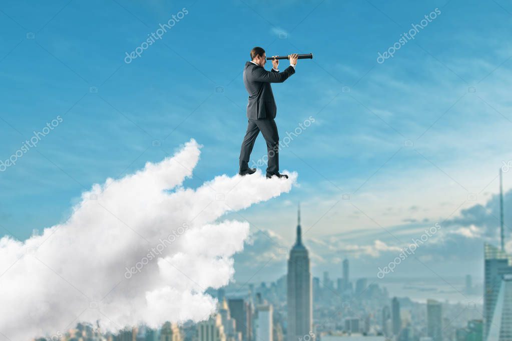 Young businessman using telescope while standing on pointing cloud hand on New York city background. Vision and success concept 