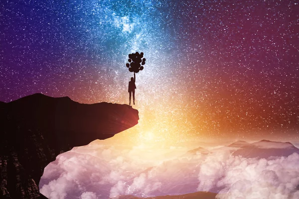 Back view of young backlit businesswoman flying with balloons on abstract starry sky space and cliff background. Freedom and fantasy concept