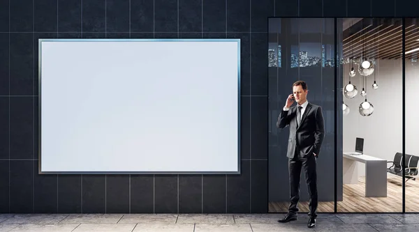 Geschäftsmann telefoniert in der Nähe eines leeren weißen Banners an einer Wand des Business Centers. — Stockfoto