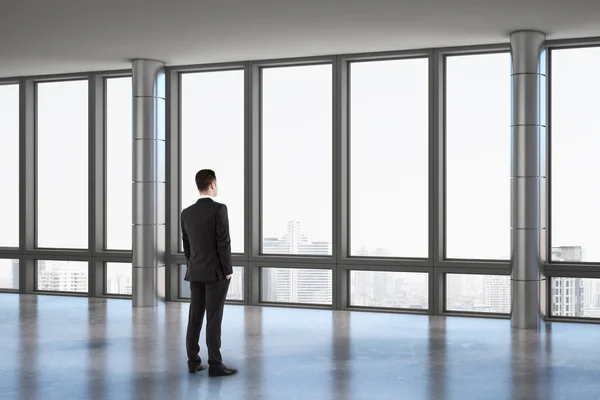 Επιχειρηματίας κοιτάζοντας μέσα από μεγάλο παράθυρο σε σύγχρονο βιομηχανικό στυλ ευρύχωρη αίθουσα. — Φωτογραφία Αρχείου