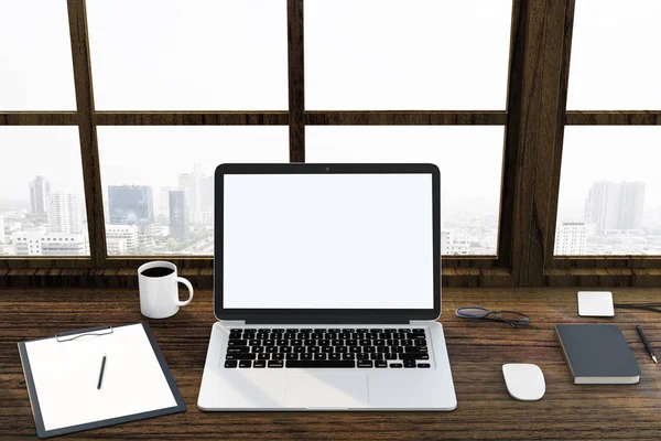 Blanco en blanco se burlan de la pantalla del ordenador portátil, taza de café y vasos en la mesa de madera con ventana de vista de la ciudad . — Foto de Stock