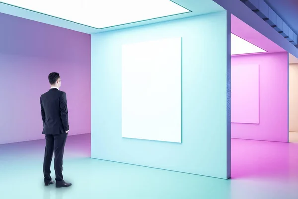 Businessman looking on blank poster on wall in gallery interior. Performance and presentation concept.