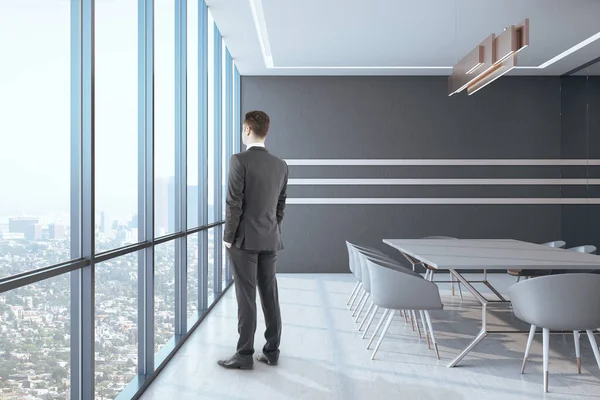 Businessman standing in meeting room with panoramic city view and meeting table. Occupation and worker concept.