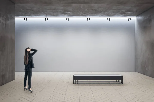Businesswoman in exhibition hall interior looking on blank wall. Gallery and presentation concept.  Mock up,