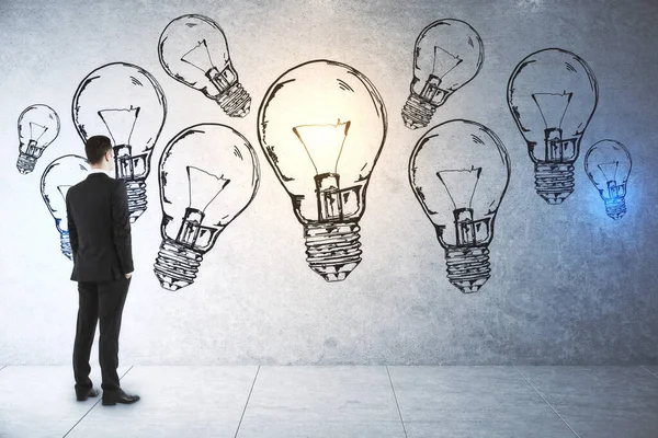 Businessman in suit looking on drawing light bulbs on concrete wall. Success and startup concept.