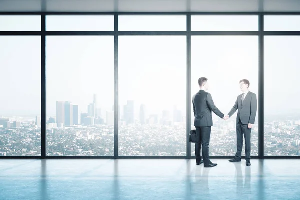 Business partners handshaking in office hall with city view. Business and teamwork concept.