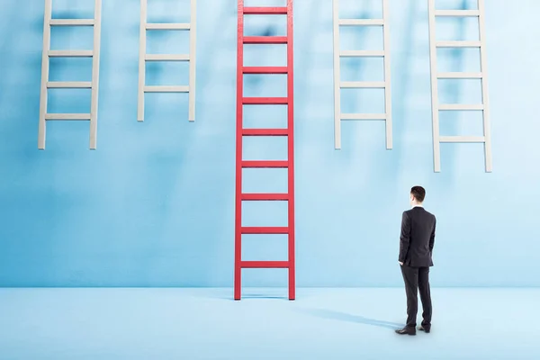 Biznesmen Garniturze Stojący Niebieskim Wnętrzu Patrzący Czerwoną Drabinę Koncepcja Sukcesu — Zdjęcie stockowe