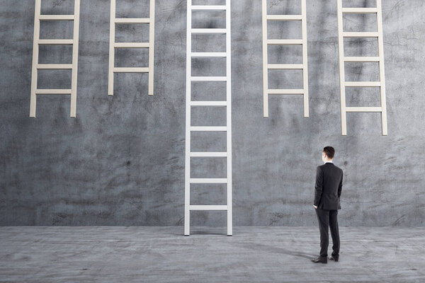 Businessman in suit standing in concrete interior and looking on wooden ladder. Success and startup concept.
