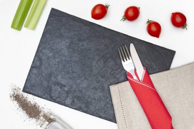 Beyaz arka planda siyah taş tahta, sebze ve çatal bıçak takımı.