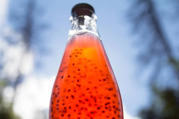 A glass bottle of orange drink. Metal stopper. Seeds inside.