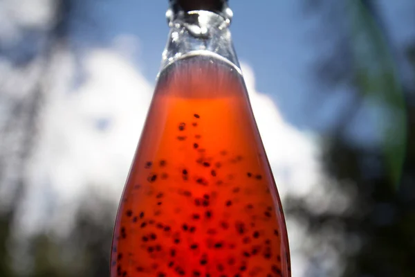 A glass bottle of orange drink. Metal stopper. Seeds inside.