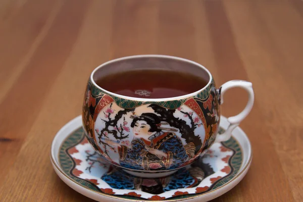 Chinese Cup with tea on a saucer. On a wooden table.