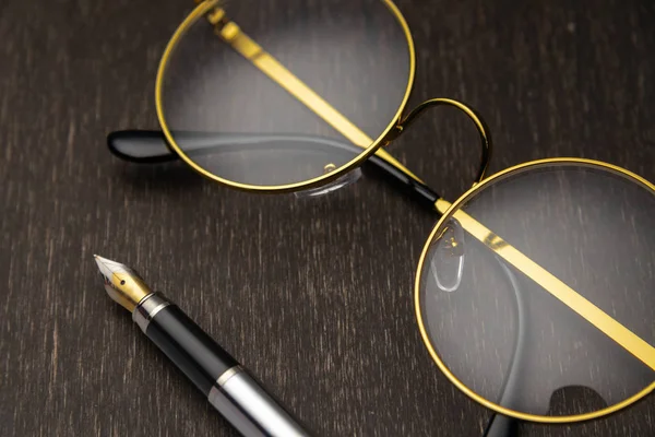 Золотые очки, ручка на темном деревянном фоне — стоковое фото