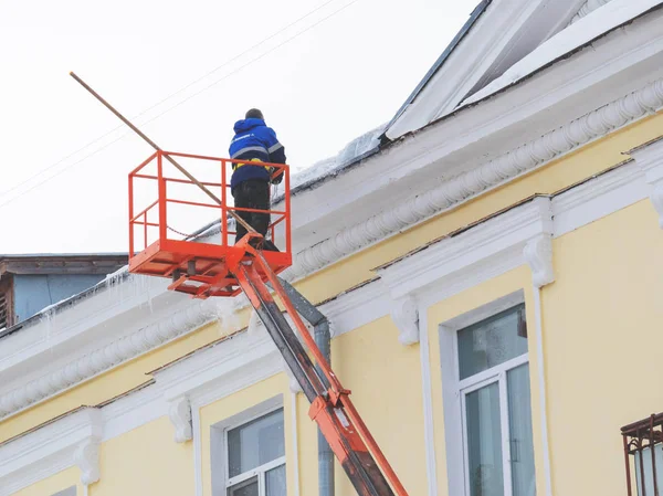 Werknemer verwijdert sneeuw en ijs van het dak van het gebouw. — Stockfoto