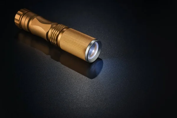 Goldene Taschenlampe auf dunkler Oberfläche. — Stockfoto