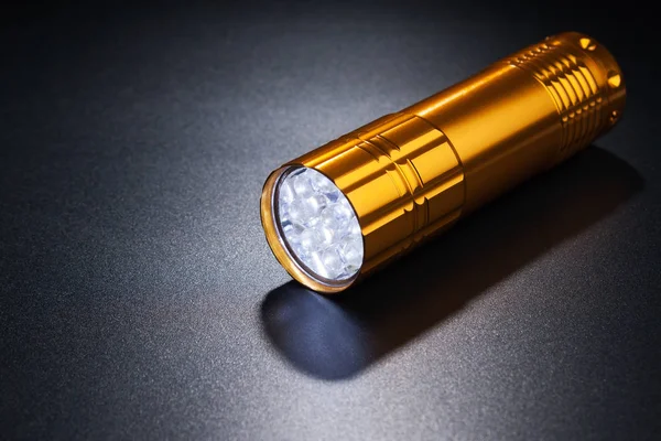 Goldene Taschenlampe auf dunkler Oberfläche. — Stockfoto
