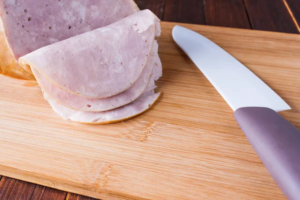Sliced ham with a ceramic knife on cutting board. — Stock Photo, Image