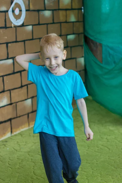 Niño alegre está jugando en el centro de entretenimiento. Él sostiene su mano detrás de su cabeza . — Foto de Stock