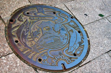 Sapporo (Sapporo-shi), Hokkaido, Japonya - 3 Eylül 2009 - Sapporo 'nun lağım kapağı Sapporo Saat Kulesi ve şehrin sembolü olarak somon balığı oyması