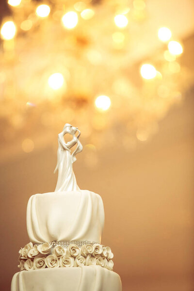 Bride and Groom wedding dolls decorated on wedding cake with bokeh of chandelier light in background