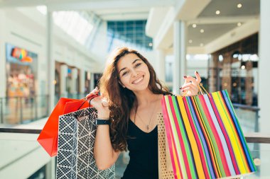 Markette yürürken renkli alışveriş torbaları taşıyan şık siyah elbiseli neşeli bir bayan. Çekici esmer, alışveriş merkezinden alışveriş yaptıktan sonra tatmin olmuş görünüyor..