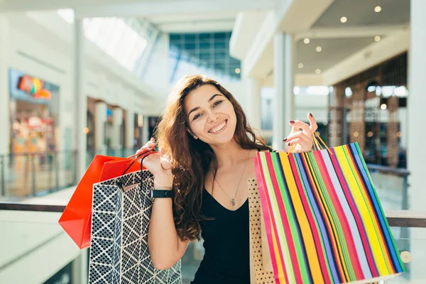 お店を歩いている間にカラフルなショッピングバッグを運ぶスタイリッシュな黒のドレスで陽気な女性 魅力的なブルネット見る満足後ショッピングでモール — ストック写真