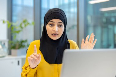 Modern bir ofisteki bir video konferansında tesettürlü genç bir iş kadını etkileyici bir iletişim ve profesyonel bir ilişki sergiliyor.