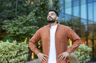 Kendine güvenen Hintli yönetici derin bir nefes alıyor, yeşil kentsel alanda temiz havanın tadını çıkarıyor, şirket ortamında farkındalığı ve iş-yaşam dengesini teşvik ediyor.