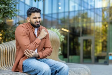 Ofis çalışanı, açık hava bankında otururken ciddi bir dirsek ağrısı yaşıyor. Yaralanma, artrit ya da diğer sağlık sorunları yüzünden.