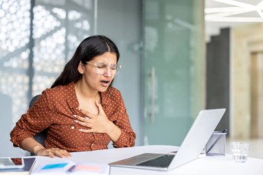 Ofis masasında çalışırken astım krizi geçiren genç bir iş kadını solunum güçlükleriyle boğuşuyor ve solunum sağlığının zorluklarını vurguluyor.
