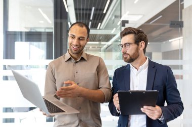 Modern bir ofiste dizüstü bilgisayarla iş birliği yapan iki işadamı, takım çalışmasının özünü ve kurumsal bir ortamda etkili iletişimin önemini vurguladılar.