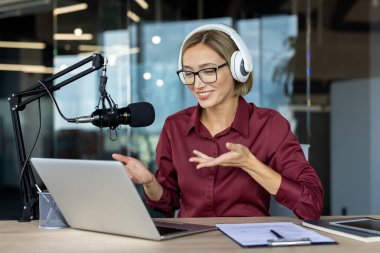 Profesyonel bir kayıt stüdyosundaki dizüstü bilgisayar kullanarak dinleyicileriyle konuşurken kulaklık takan ve mikrofona konuşan bir bayan radyo karakteri.
