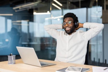 Kulaklık takan ve elinde not defteri tutan mutlu bir kadın, online toplantıda rahat bir oturma odasında kanepede otururken dizüstü bilgisayar kullanarak konuşuyor..