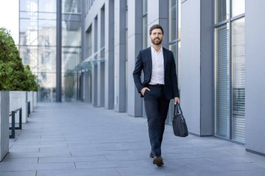 Modern bir ofis binasının dışında yürüyen kendine güvenen bir işadamı, işe giderken bir evrak çantası taşıyor, profesyonellik ve hırsı somutlaştırıyor.