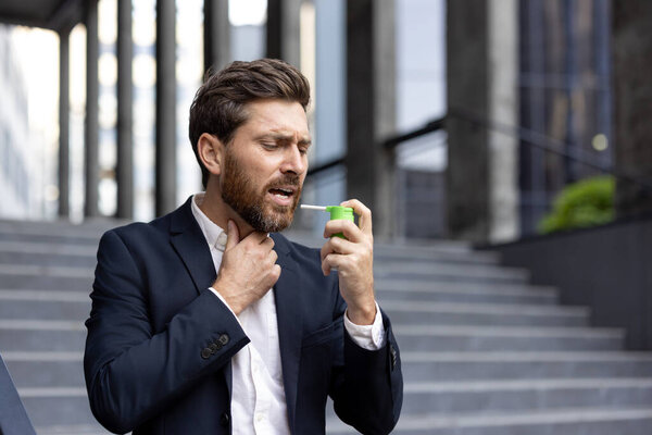 Sick man uses spray to relieve sore throat. Mature businessman suffers from sore throat and inflammation of the throat.