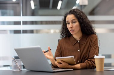 İş kadını önemli bir çevrimiçi video görüşmesi yapıyor. Modern bir ofisteki bilgisayarında çalışıyor. Uzaktan kumanda sırasında iletişim kuruyor ve tartışıyor.