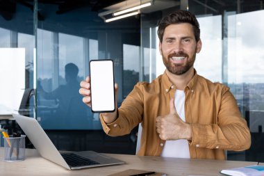 Modern bir ofiste gülümseyen bir işadamı elinde boş ekranlı bir akıllı telefon tutarak başparmak kaldırıyor, mobil bir uygulama sunuyor ve onay ve başarı sinyalleri veriyor.