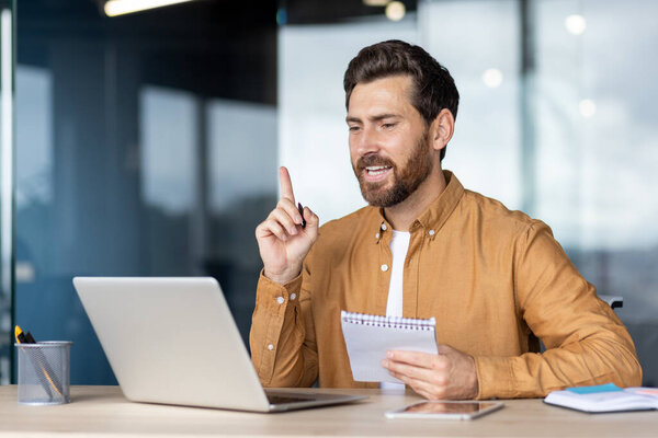 Confident bearded man brainstorming, having an idea, and explaining a concept during a remote video conference meeting using his laptop in a modern office